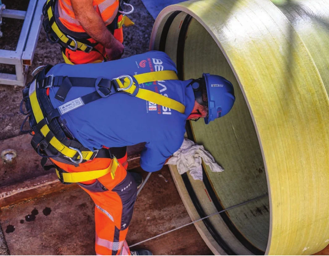 Operatori con casco e imbracatura lavorano in corrispondenza del bordo di un tubo di grande diametro.