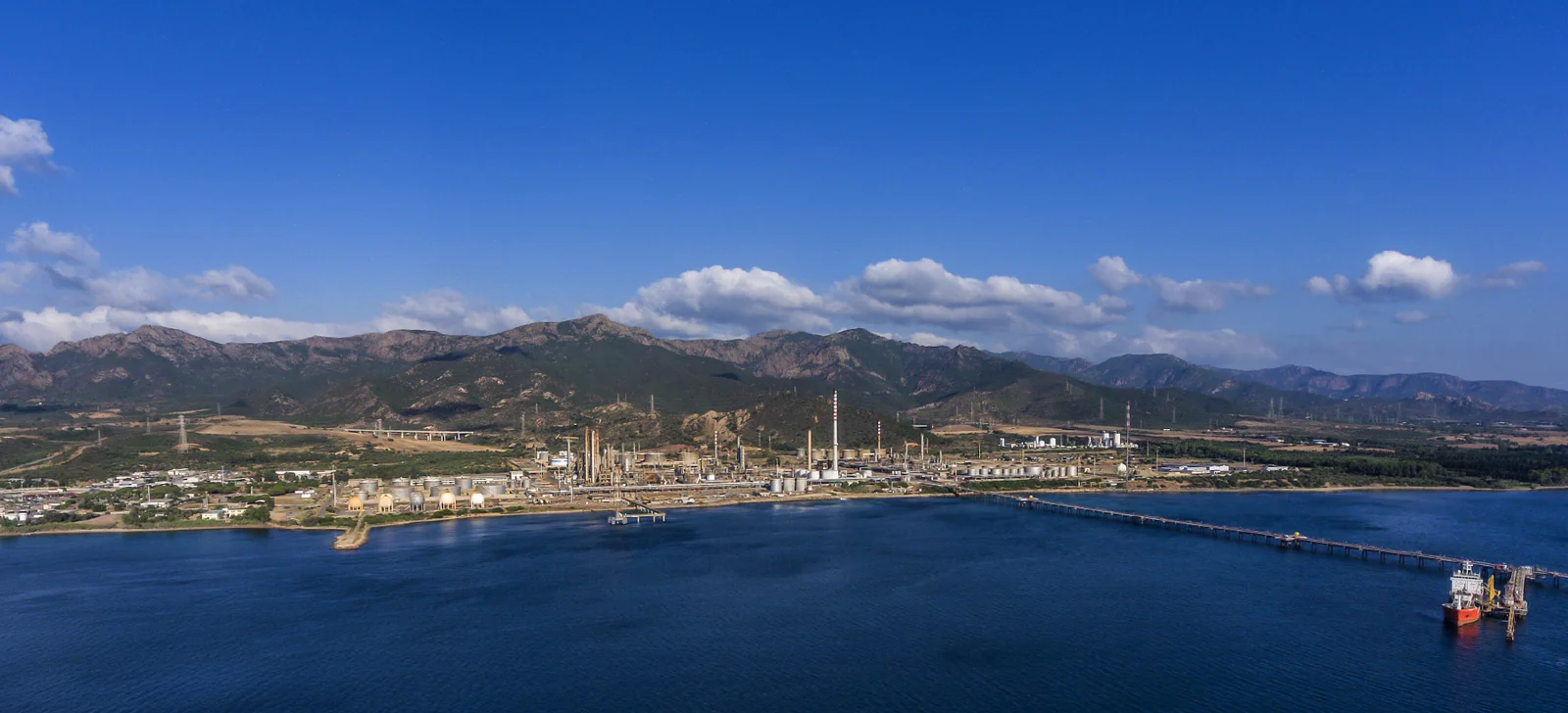 Veduta dal mare di un impianto industriale lungo la costa, con rilievi sullo sfondo