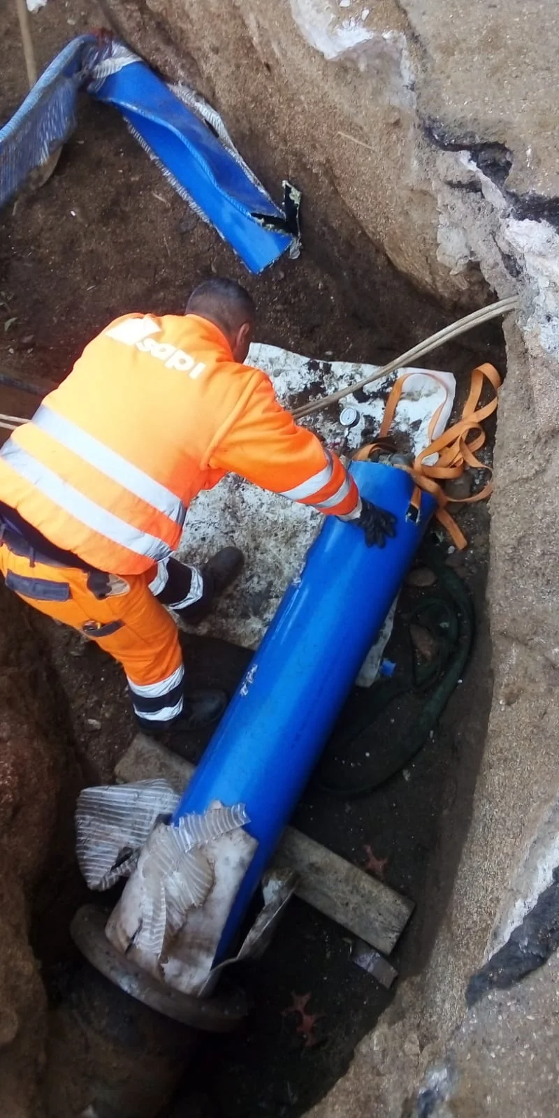 Operatore in arancione al lavoro su un raccordo cilindrico blu all’interno di uno scavo.