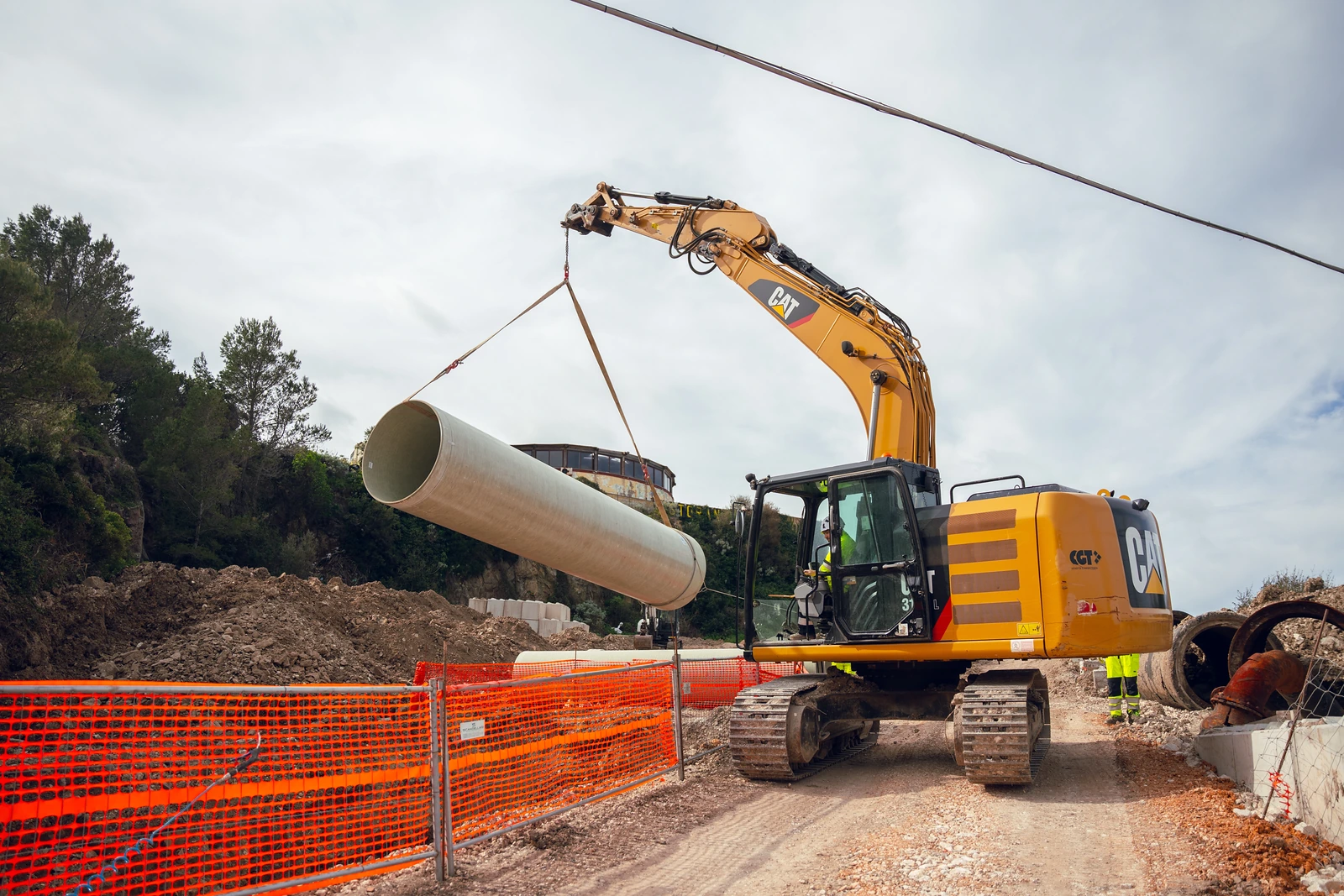Escavatore che solleva una sezione di tubo chiaro con fasce nel cantiere